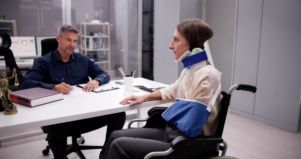 Attorney meeting with a client in a wheelchair wearing a neck brace and arm sling