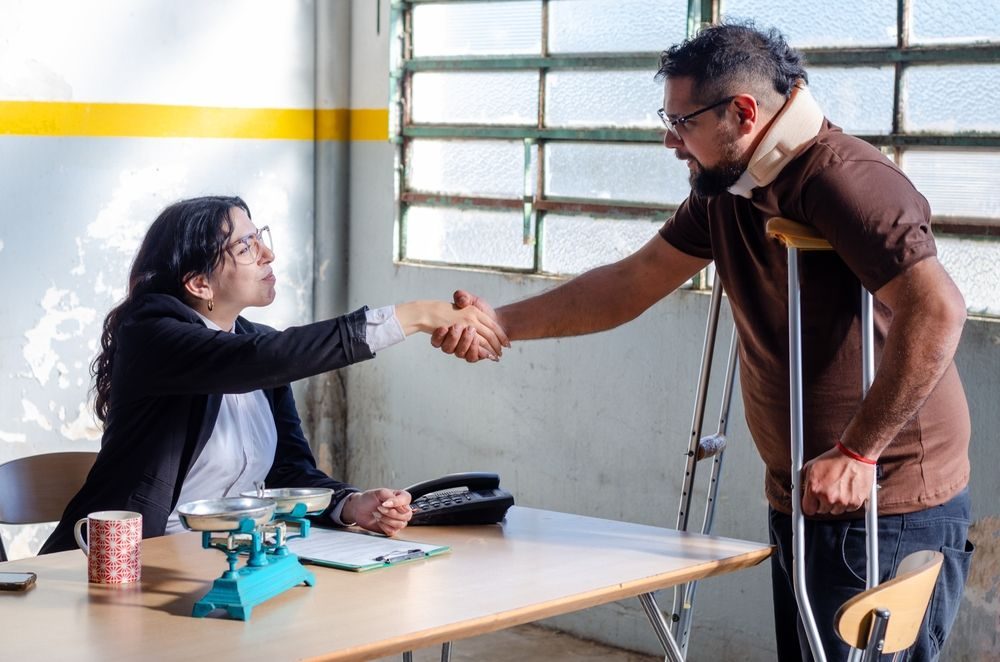 Abogado de discapacidad dándose la mano con un cliente que usa collarín y muletas