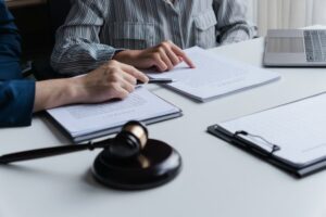 Two people reviewing printed documents at a desk, one pointing with a pen, with a wooden gavel in the foreground