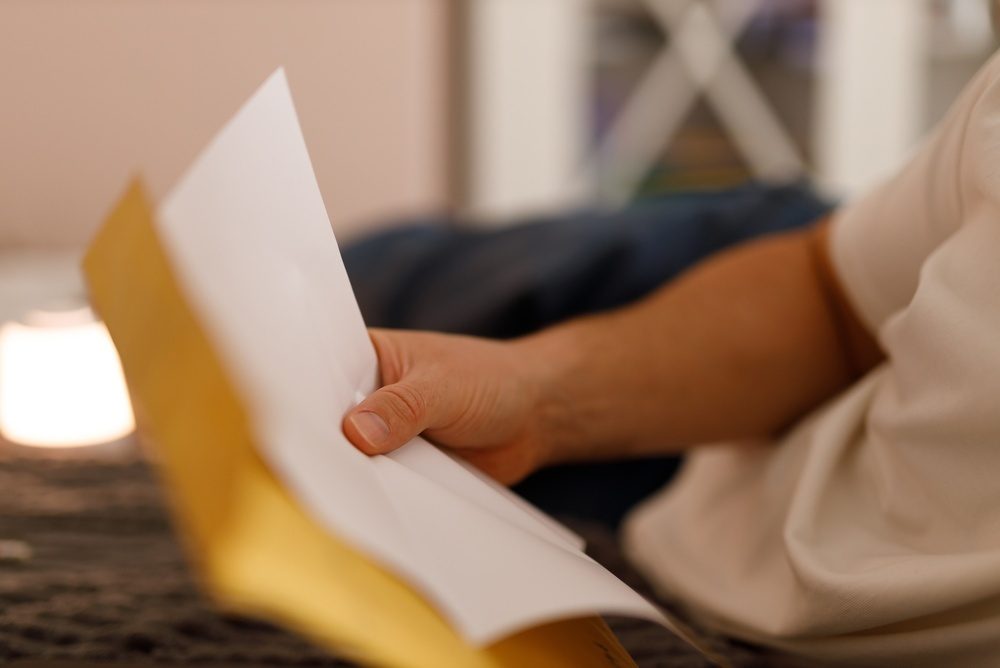 Close-up of a hand pulling a folded letter out of a yellow envelope